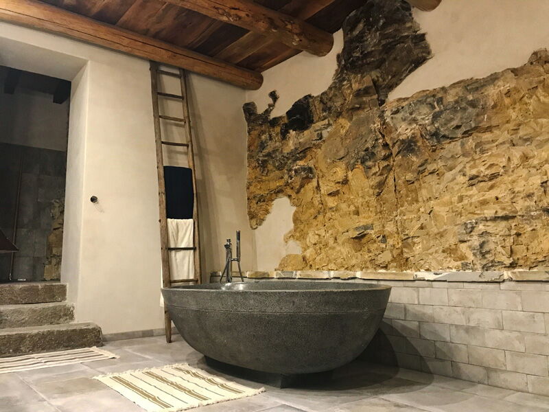Bad mit Natursteinwand, freistehender Badewanne und weißem Naturkalkputz