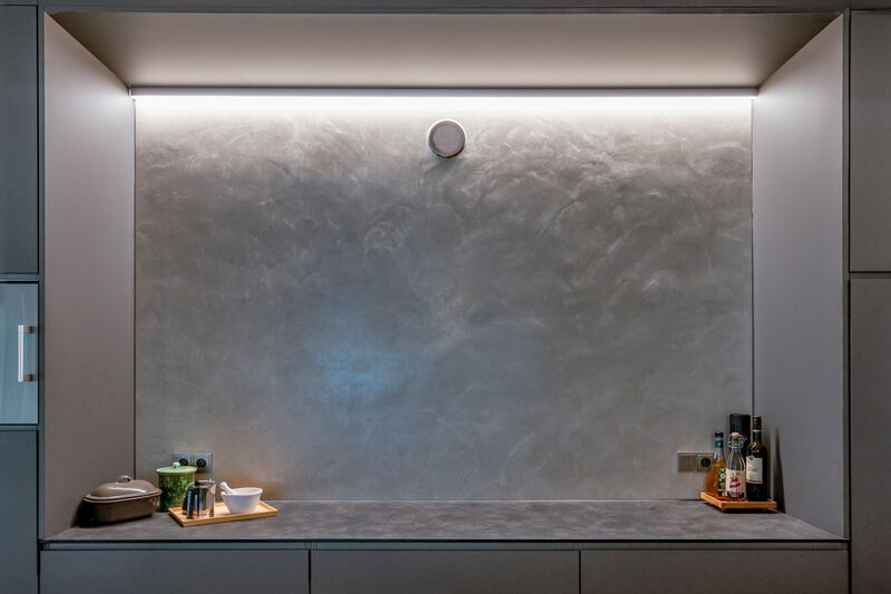 Moderne Küche mit grauer Naturkalkputz-Wand, indirekter Beleuchtung und Arbeitsfläche