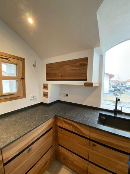 Kitchen area with wooden cabinetry, natural stone countertop and white natural lime plaster